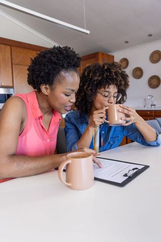 Black women reviewing paperwork over coffee at kitchen table collaborating on finances