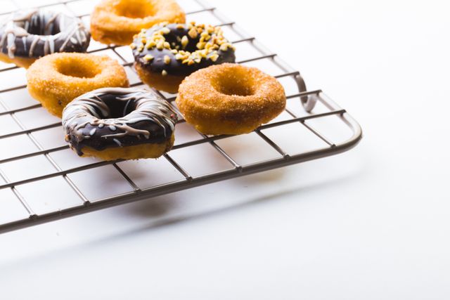 High angle view of fresh various donuts on cooling rack against white background. unaltered, unhealthy eating and sweet food concept.
