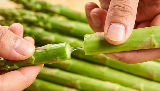 Hands breaking fresh asparagus spears with visible sap droplet close-up kitchen prep raw