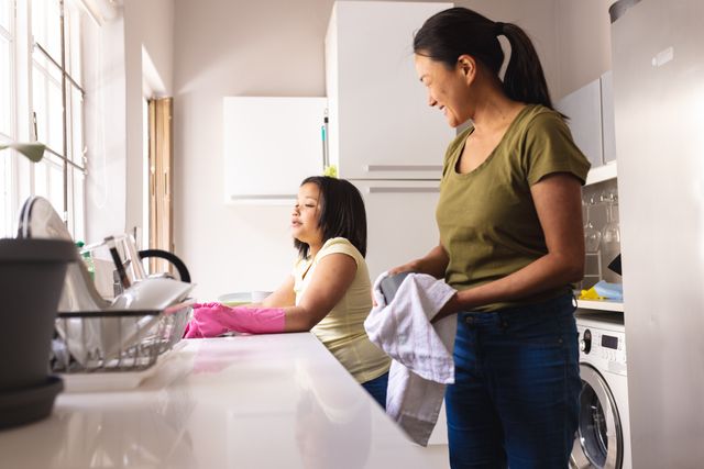 Happy asian mother and daughter washing and drying dishes together in kitchen at home, copy space. Domestic life, family, togetherness, inclusivity and lifestyle.