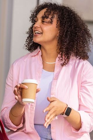 African american woman holding coffee cup and chatting in pink shirt, casual friendly portrait