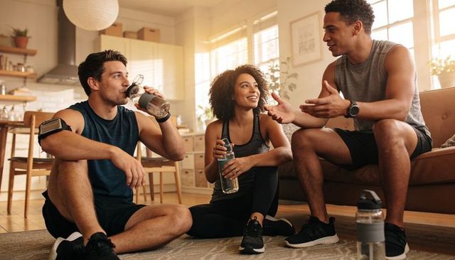 Friends chatting and resting after home workout with water bottles in sunlit living room