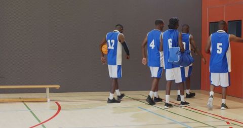 Basketball team walking off indoor court after game wearing blue jerseys and carrying ball and bag