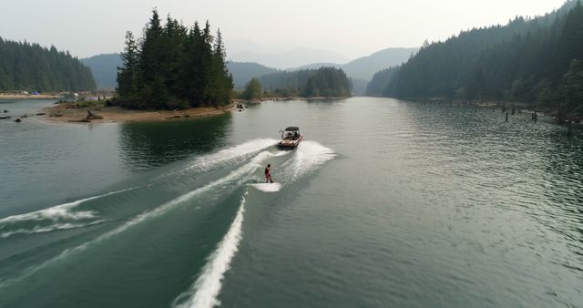 A person engages in waterskiing behind a boat on a serene lake surrounded by forested mountains, with copy space. Waterskiing offers an exhilarating experience, combining the thrill of speed with the beauty of natural landscapes.
