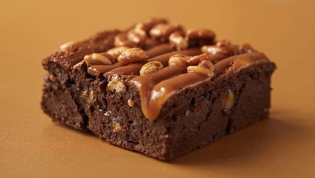 Dripping caramel pecan brownie on fudgy chocolate square, glossy indulgent dessert