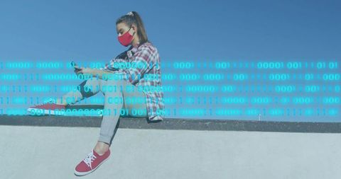 Young woman wearing red face mask checking smartphone on rooftop ledge with binary overlay