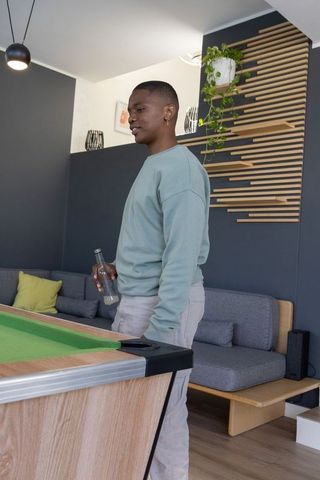 African american man standing by pool table holding bottle in modern lounge interior