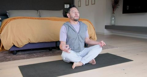Mature Man Meditating on Yoga Mat in Contemporary Bedroom