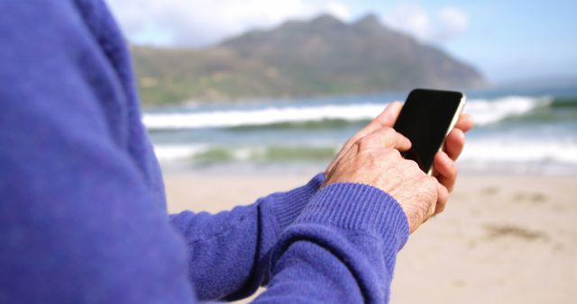 Senior Using Smartphone on the Beach with Sea Waves and Mountains - Download Free Stock Images Pikwizard.com