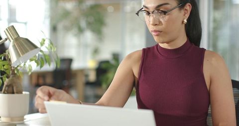 Professional woman working on laptop in modern open-plan office with natural greenery