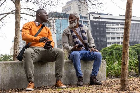 African american friends sitting and chatting on concrete bench in urban park cityscape