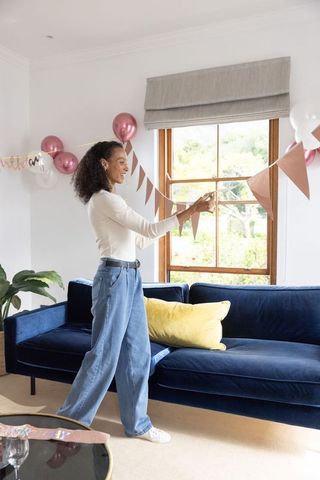 Hanging rose gold bunting across window in living room with velvet navy sofa and balloons
