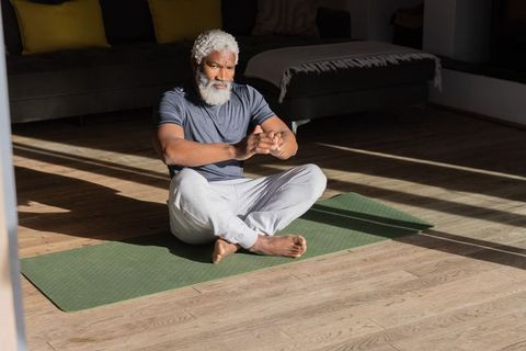 Senior african american man practicing seated stretch on yoga mat in sunlit living room