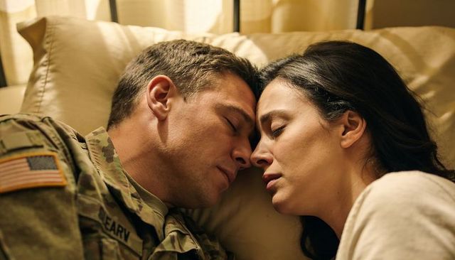 Soldier returning home sharing tender bedside moment with partner in warm evening light