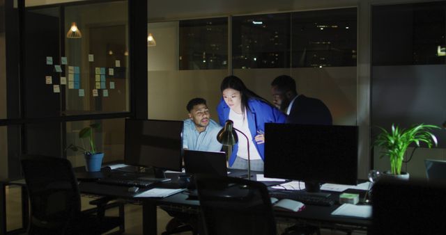 Image of three happy diverse male and female colleagues using computers talking at night in office. Business, communication, inclusivity and flexible working concept digitally generated image.