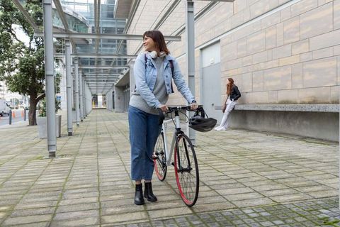 Diverse woman pushing bicycle along urban plaza while friend leaning and checking phone