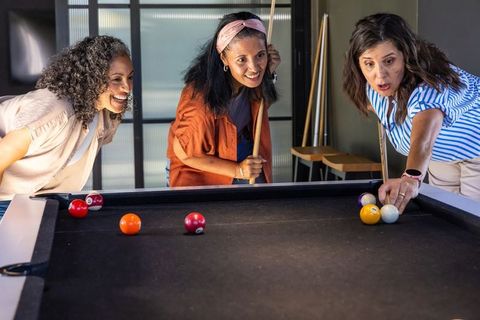 African american women lining up pool shot at black felt table, friends enjoying billiards night