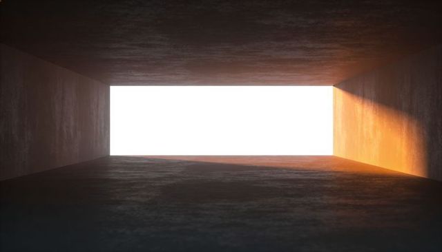 Framing rectangular exit revealing bright white light and warm sunlit patch on concrete wall