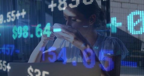 Sipping coffee while analyzing stock market data on laptop with blue digital overlay