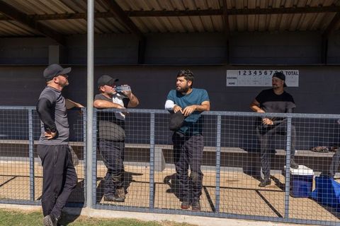 Male teammates chatting and drinking water in dugout during amateur baseball game