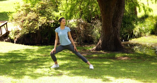 A woman practicing yoga in a serene park setting, surrounded by greenery and calm natural elements. She is stretching and focusing on her fitness and wellbeing. Ideal for promoting a healthy lifestyle, fitness routines, outdoor activities, and balance between mind and body. Useful for fitness blogs, wellness websites, and outdoor activity advertisements.