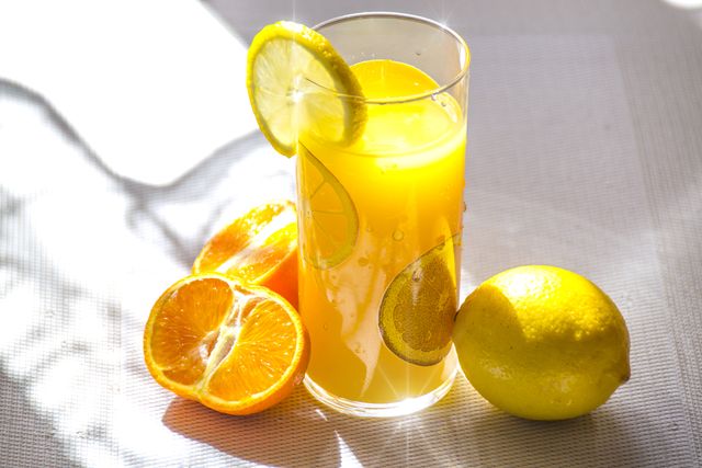Refreshing citrus juice in a tall glass with lemon and orange slices, catching sunlight. Ideal for promoting wellness, detox drinks, summer refreshments. Perfect for use in health blogs, food and drink websites, and advertisements for beverages.