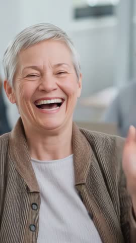 Senior woman laughing and waving during video call in office vertical portrait clip