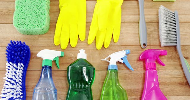 A variety of cleaning supplies, including gloves, brushes, and spray bottles, are neatly arranged on a wooden surface, with copy space. These items are essential for maintaining cleanliness and hygiene in both residential and commercial settings.