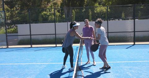 Women shaking hands at net after pickleball match on bright blue outdoor court