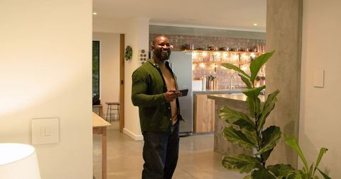 African american man smiling while holding smartphone in modern open-plan kitchen