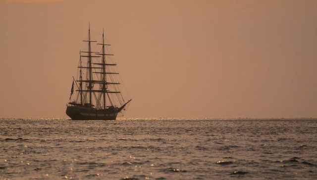 Majestic three-masted ship transitioning ocean at golden sunset