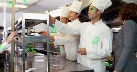 Chefs plating dishes on pass while manager overseeing busy industrial restaurant kitchen