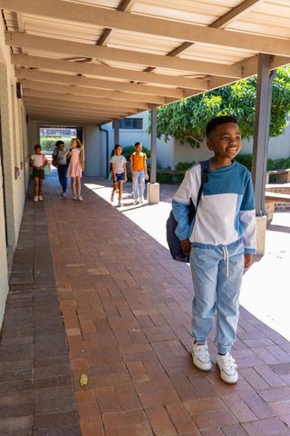 Smiling african american boy standing with backpack on school walkway under canopy