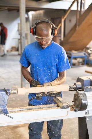 African american woodworker shaping lathe-turned spindle wearing safety goggles and ear muffs