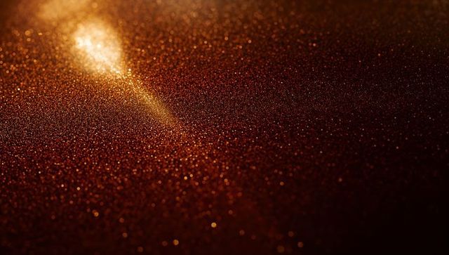 Golden glitter bokeh macro background with warm metallic sparkle and amber light flare