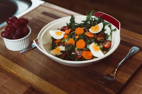Serving mixed salad with boiled egg, arugula, carrots and cherry tomatoes on wooden board