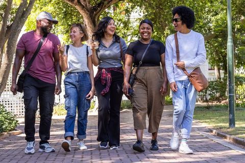 Friends walking together on sunlit park path laughing and carrying coffee
