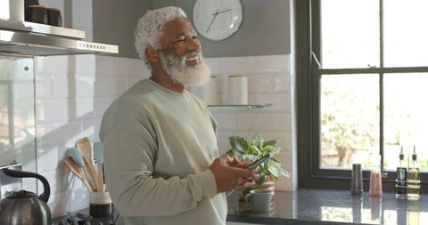 Senior Man Smiling in Modern Kitchen Holding Smartphone