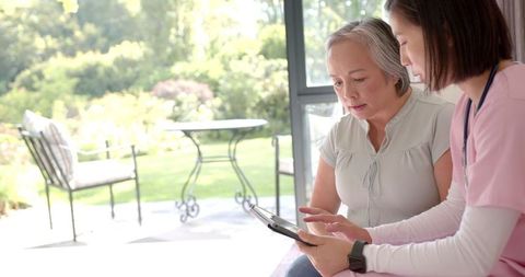 Physiotherapist guiding senior woman with tablet exercises at home
