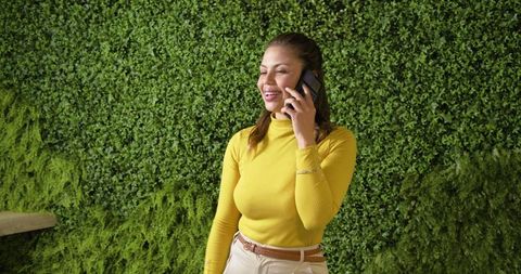 Middle-aged woman talking on smartphone beside living green wall in modern lobby