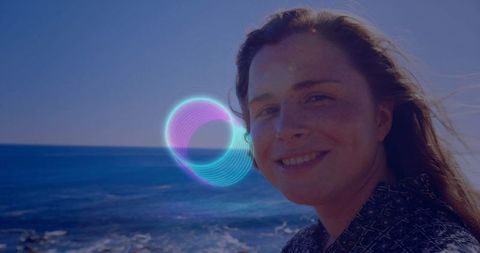 Smiling woman by ocean with futuristic neon light overlay