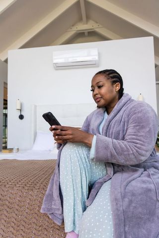 African american woman relaxing in lavender robe and polka dot pajamas using smartphone