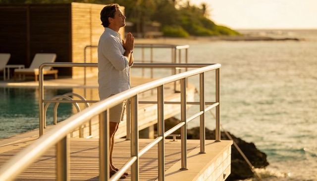 Man meditating on resort deck at sunset over ocean | mindfulness, wellness retreat