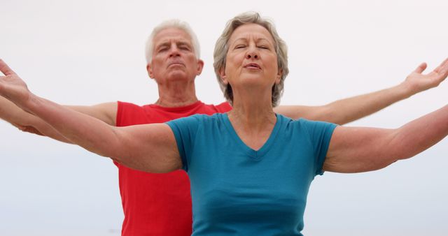 Senior couple practicing yoga outdoors with arms open, focusing on health and wellness. Ideal for use in wellness blogs, fitness magazines, articles about healthy aging, or promotional materials for senior fitness programs.