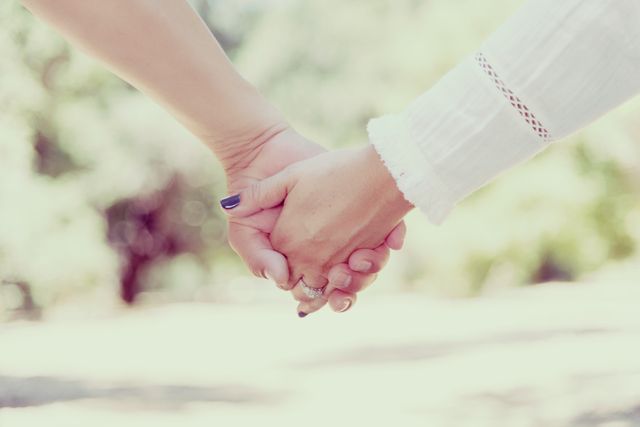 Close-up image of a couple holding hands, showcasing their engagement rings. Suitable for illustrating themes of love, romance, engagements, relationships, and unity. Ideal for wedding announcements, relationship advice articles, and romantic promotional materials.