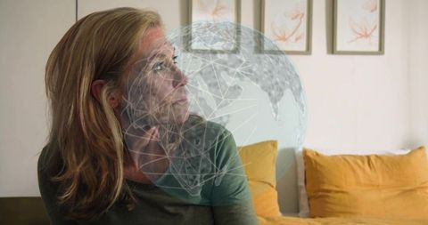 Mature woman gazing at holographic globe overlay in cozy bedroom, digital connectivity