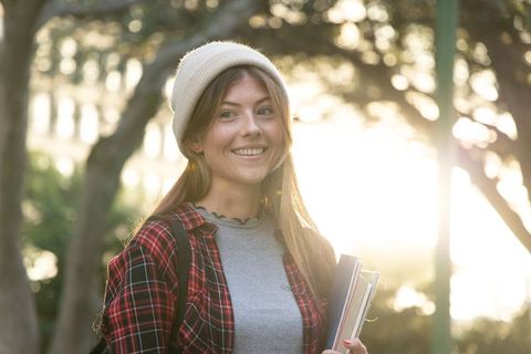 Smiling teenage student holding books on campus during golden hour backlit portrait