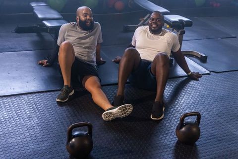 African american men resting after workout, smiling and bonding in gym with kettlebells
