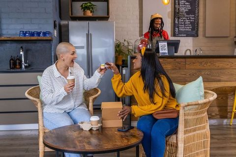Two friends sharing coffee and cupcake in cozy rustic cafe, mustard knit sweater