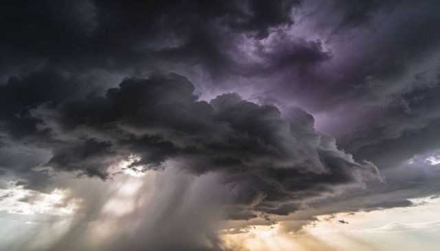 Dramatic cumulonimbus storm dropping heavy rain shaft while sunbeams pierce dark clouds